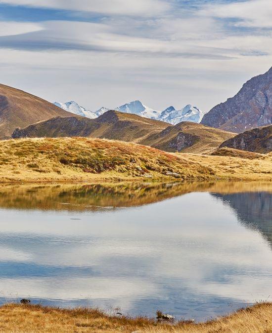 Alpine lake reflecting mountain peaks under a partly cloudy sky in autumn