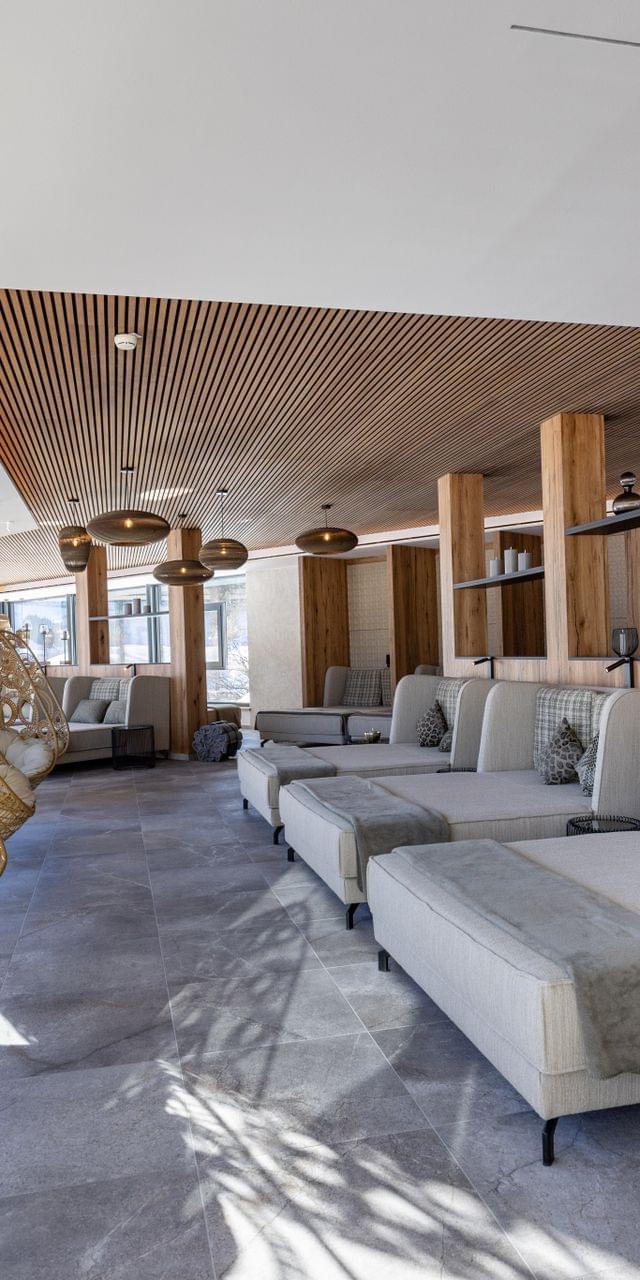 Badehaus Ruheraum mit Großen Liegen und Schwingsesseln vor Panorama-Fenster und Blick auf die verschneite Bergwelt 